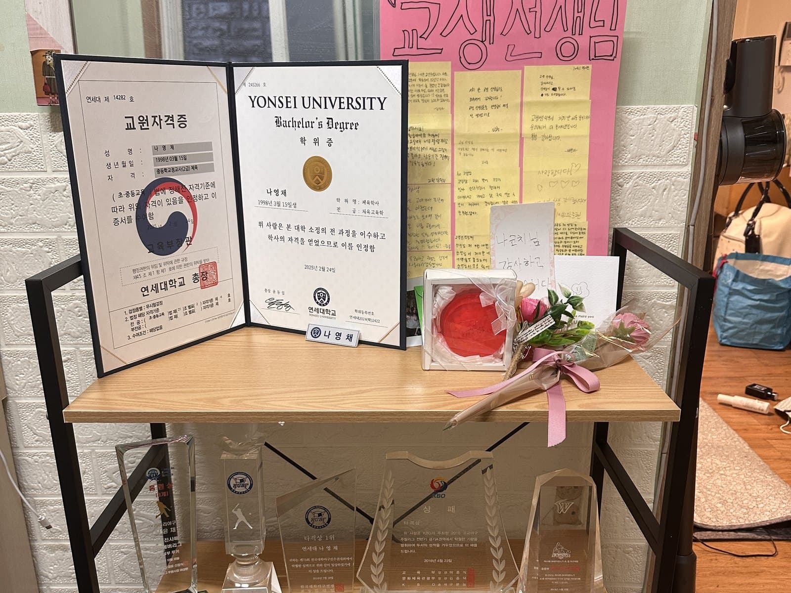교원자격증과 학위증, 꽃다발과 「교생선생님」이라고 쓴 종이가 놓인 선반